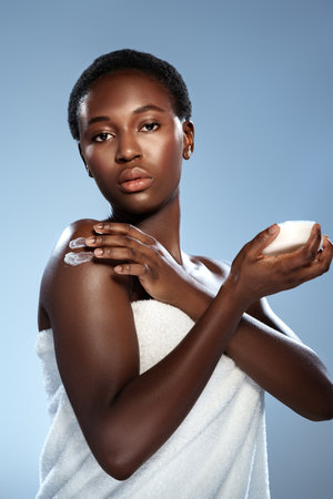 Woman applying skin cream during a skincare routine with a soft towel in a calming studio environmentの写真素材