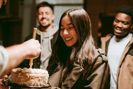 Friends celebrate a birthday with laughter and cake in a cozy indoor setting during a joyful evening gatheringの写真素材