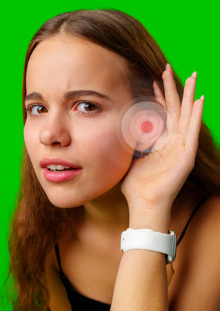 Young woman listening intently with hand to ear against bright green background, showcasing curiosity and engagement in the momentの写真素材