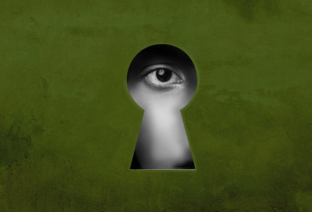 Mysterious gaze through a keyhole revealing an eye watching the world in a dimly lit environmentの写真素材
