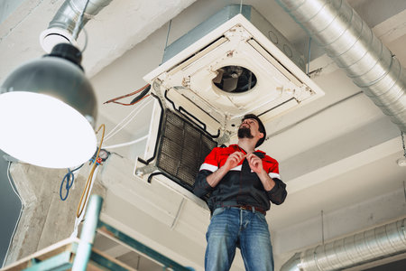 Technician repairs air conditioning unit in modern office space during daylight hoursの写真素材