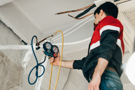 Technician conducts maintenance on air conditioning system in modern facility with gauges and hoses for accurate readingsの写真素材
