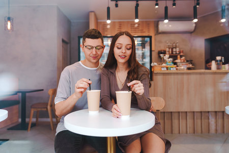 Young couple enjoying warm drinks at a cozy cafe in the afternoon, sharing a moment together in a welcoming atmosphereの写真素材