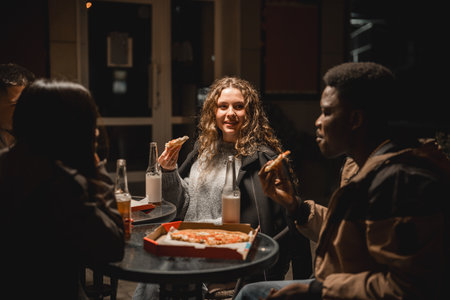 Group of friends enjoying pizza and drinks at night outside in a cozy urban settingの写真素材