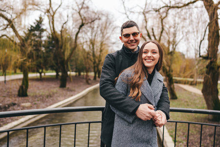 Couple enjoys a joyful moment on a bridge in a tranquil park during the early spring afternoonの写真素材