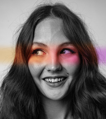 Young woman with long hair smiling and colorful paint stripes on her face in a creative studio settingの写真素材