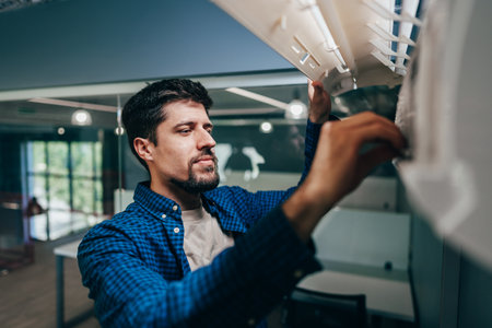 Focused worker adjusting equipment in a modern office setting during the dayの写真素材
