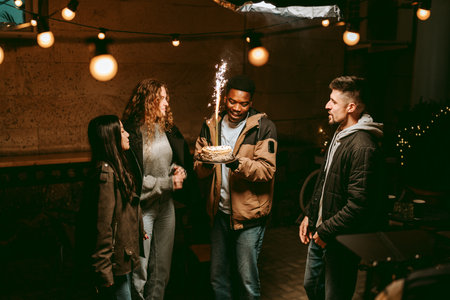 Friends celebrate a birthday outdoors at night with sparklers and festive lights in a lively...