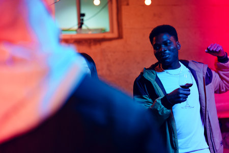 Man enjoying a lively indoor party while holding a glass of red wine in a vibrant atmosphere with colorful lightingの写真素材