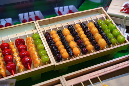 Delicious dessert skewers displayed at a bustling market during an evening food festivalの写真素材