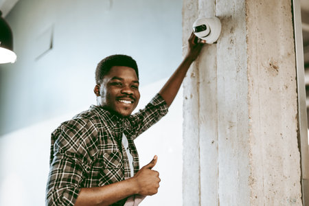 Man installing security camera in modern office space while smiling and giving thumbs upの写真素材
