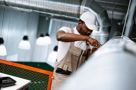 Worker performs maintenance on ventilation system in modern industrial space during daylight hoursの写真素材