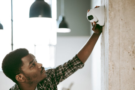 Technician installs security camera on a concrete wall in a modern office environment during daytime hoursの写真素材