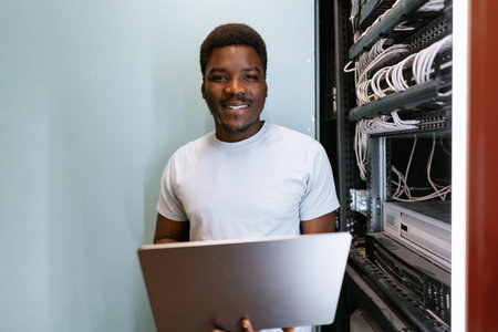 Young technician working in server room, managing cables and technology efficiently while smiling