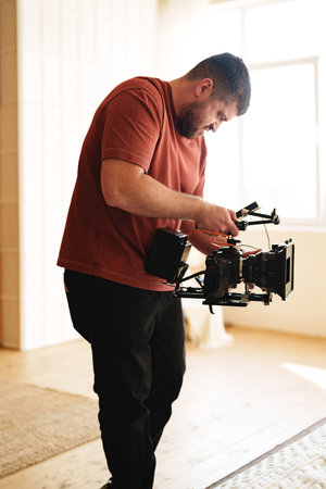 Cinematographer adjusts camera equipment in a bright, spacious room during a film shootの写真素材
