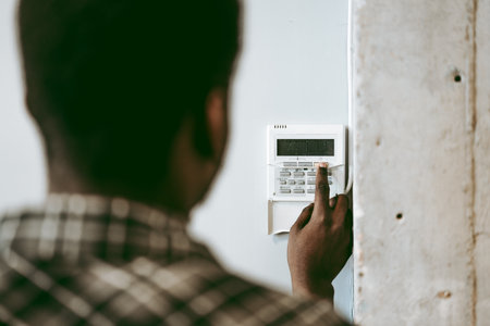 Man setting security system at home in the afternoon, focusing on keypad and monitoring device for...