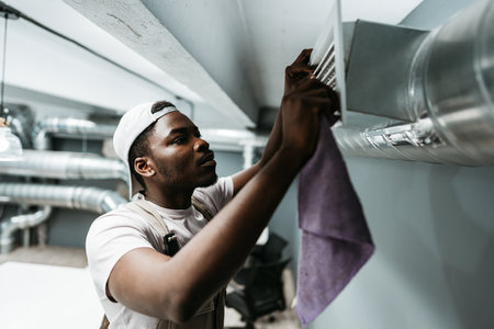 Skilled technician adjusts air vent in modern indoor space during maintenance inspection