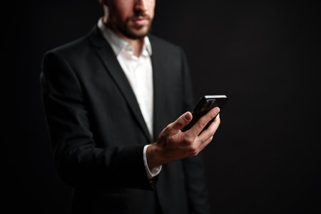 Professional man in suit using smartphone against dark background during eveningの写真素材