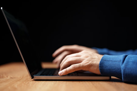 Hands typing on a laptop during evening work session in a dimly lit workspaceの写真素材