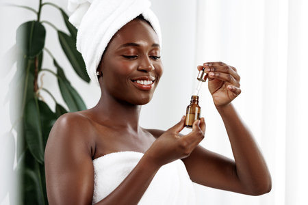 Woman applying skincare serum at home after shower, enjoying self-care routine in bright bathroomの写真素材