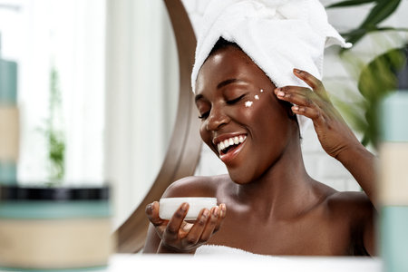Woman enjoying a skincare routine with cream and a joyful smile in a bright bathroom settingの写真素材