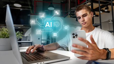 Young man engaged in artificial intelligence research while using a laptop and smartphone in a modern office spaceの写真素材