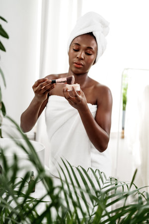 Woman applying makeup in a bright bathroom featuring plants and natural light during the dayの写真素材
