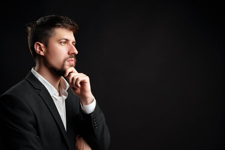 Man in a business suit contemplating ideas against a dark background in a studio settingの写真素材