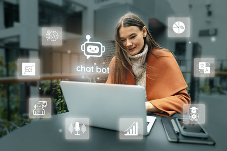 Young woman using a laptop with chatbot icons in an outdoor urban setting during daytimeの写真素材