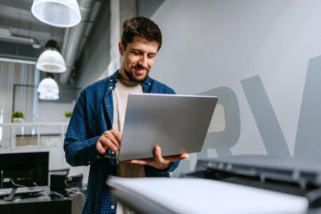 Man working on laptop in modern office environment during daytime with smiling expression