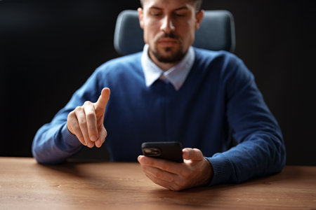 Man using smartphone while gesturing with his hand in a modern office setting during the dayの写真素材