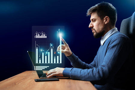 Professional man analyzing data trends and graphs on a laptop in a modern workspace at night