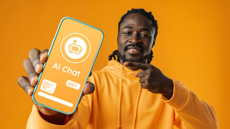 Young man excitedly shows smartphone screen displaying AI chat interface in bright orange settingの写真素材