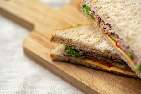 Freshly made sandwich with layers of tuna, lettuce, and cheese on a wooden cutting board at lunchtimeの写真素材