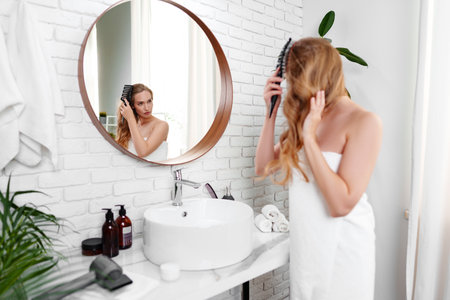 Woman applying skincare product in bathroom mirror during morning routineの写真素材