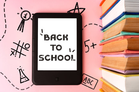 Back to school preparations with a tablet and stacked textbooks on a pink backgroundの写真素材