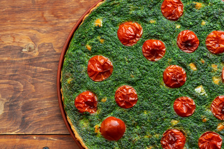 Freshly baked spinach and tomato pie on a wooden table, perfect for a healthy meal or snack in a...
