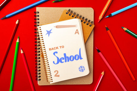 Colorful school supplies arranged on a bright red background, showcasing notebooks and colored...