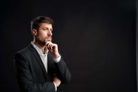 Businessman in formal suit pondering ideas against dark background in a professional setting