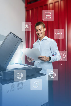 Young man smiling while using a multifunction printer for printing documents in a modern workspace