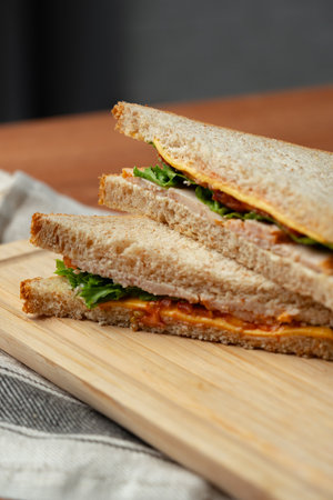 Freshly made sandwich with layers of greens and cheese on wooden cutting board