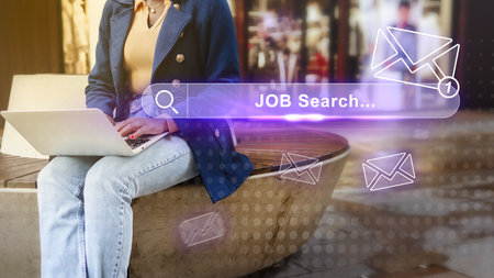 Young professional engaged in job search on laptop in urban setting during daytimeの写真素材