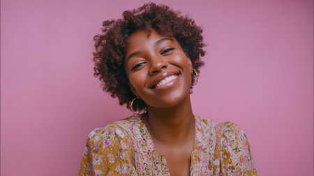 Smiling woman with curly hair wearing floral attire poses against a pink backgroundの素材