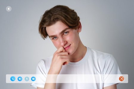Young man smiles playfully while resting his chin on his hand against a neutral backgroundの写真素材