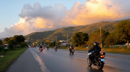 Motorcycles cruising along a scenic highway at sunset near mountains in a peaceful landscapeの素材