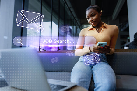 Engaging in a job search while sitting in a modern workspace and checking for updates on a mobile deviceの写真素材