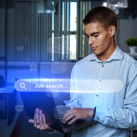 Young man engaging in job search while using laptop in modern office workspace during daytimeの写真素材