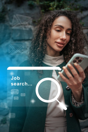 Woman engaged in job search using smartphone while wearing a stylish coat in a modern urban settingの写真素材