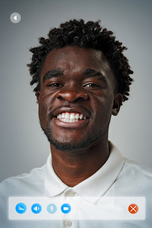 Young man smiles confidently in white polo shirt against a neutral background during a virtual...