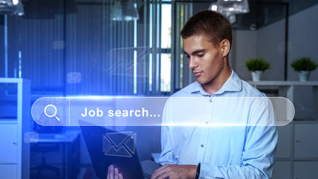 Young man conducting a job search in a modern office during the day while using a laptopの写真素材